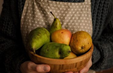 Close-up of a person holding a wooden bowl with fresh fruits including pears.
