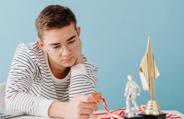 Young man with eyeglasses examines his medals and trophies, reflecting success.